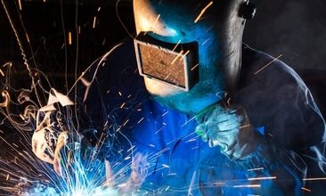 A welder is working on steel fabrication, welding metal pieces together in a factory setting.