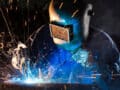 A welder is working on steel fabrication, welding metal pieces together in a factory setting.