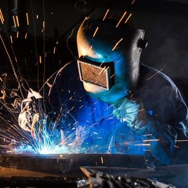 A welder is working on steel fabrication, welding metal pieces together in a factory setting.