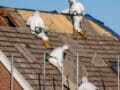 Three workers in protective clothing removing asbestos on a roof.