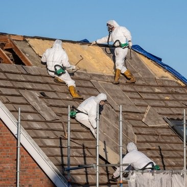 Three workers in protective clothing removing asbestos on a roof.